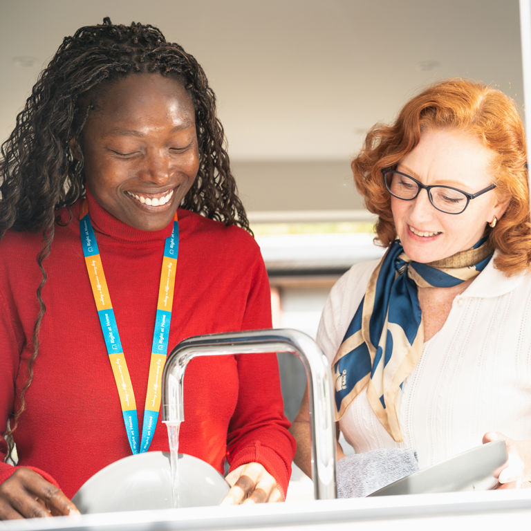 Client and carer smiling and doing the washing up together