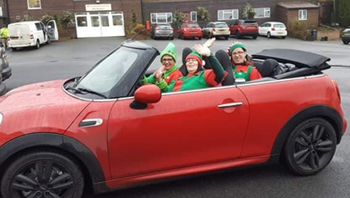 Three people dressed as elves in a red convertible mini car.