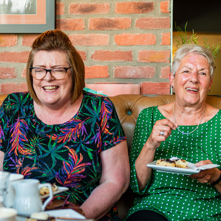 Adult daughter sitting with elderly mother in kitchen sharing tea and conversation