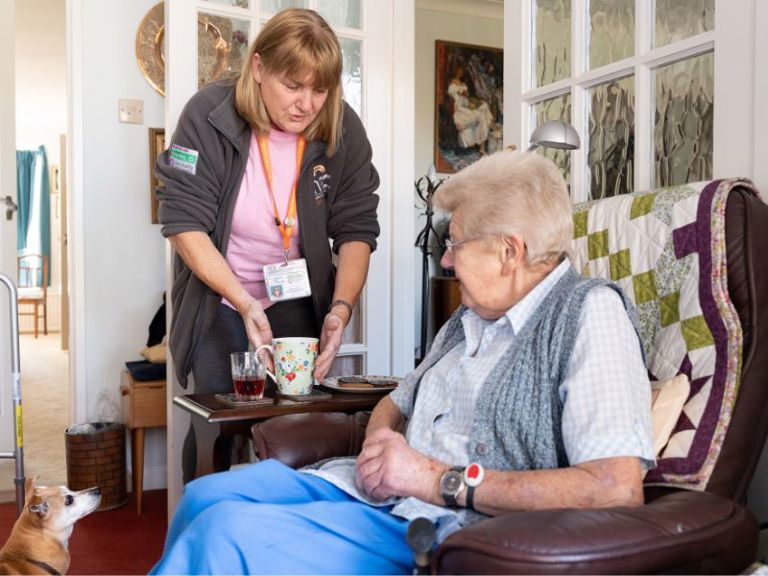 Carer serving a cup of tea to a client sitting comfortably at home.