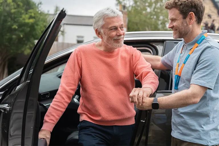 Carer supporting a client as they get out of a car after hospital discharge