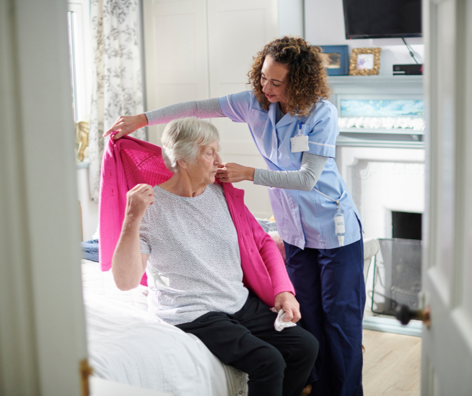A Care Assistant smiling warmly while helping an elderly client put on her jacket, showing compassionate support in a home environment