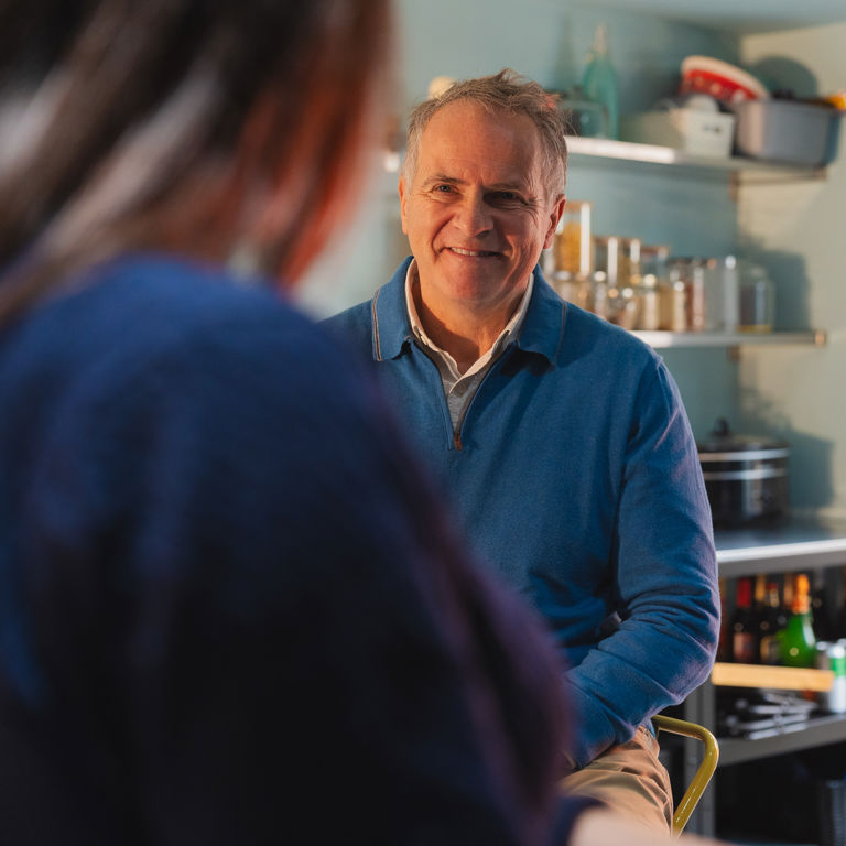 Older man smiling during conversation with caregiver in kitchen during home care visit