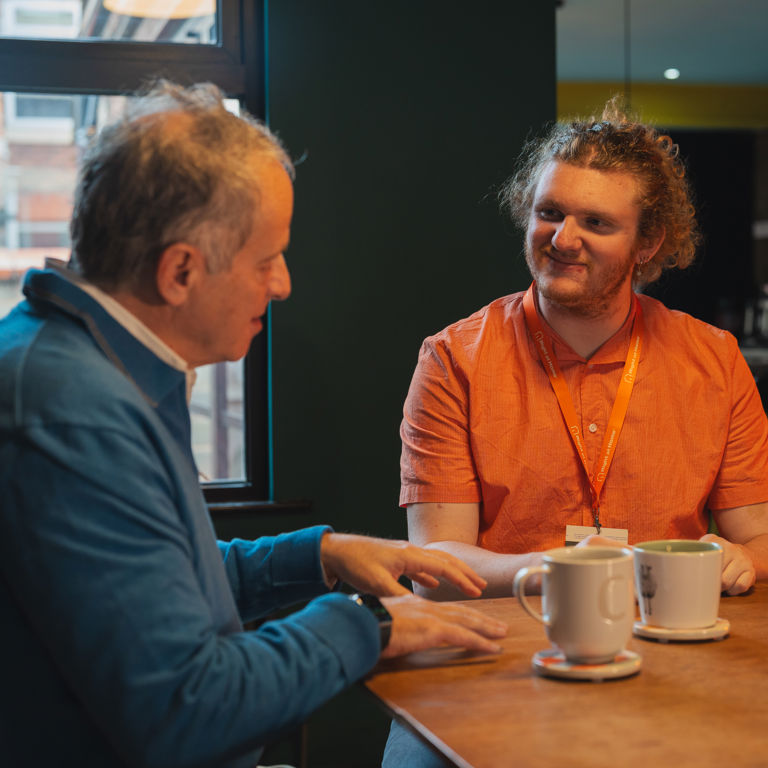 A carer sits in a cafe drinking a coffee with an elderly client