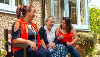 client with carers in garden on bench