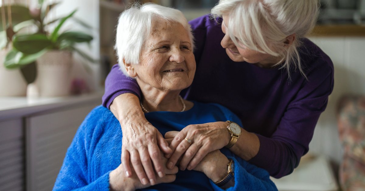 Older woman smiling as her daughter hugs her at home