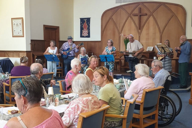 homecare clients, care professionals and volunteers enjoy afternoon tea music performance