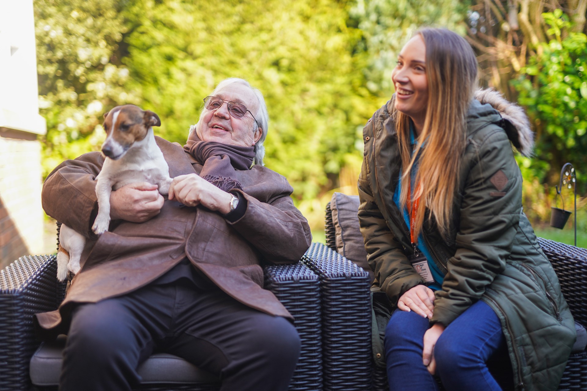 Image of an older gentleman with a dog and a carer sitting in the garden