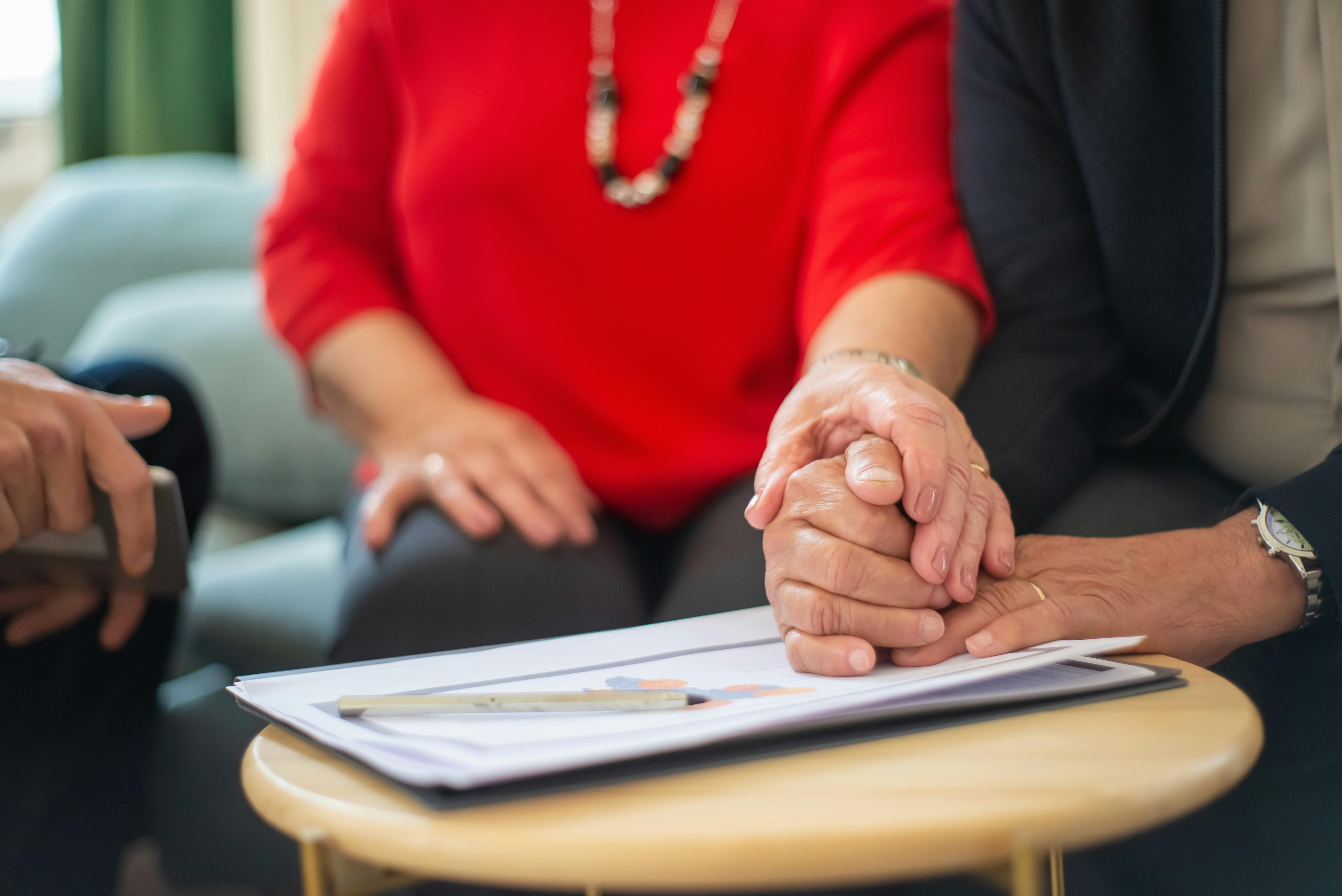 Two seniors holding hands across a table with paperwork, representing families managing Attendance Allowance and home care planning