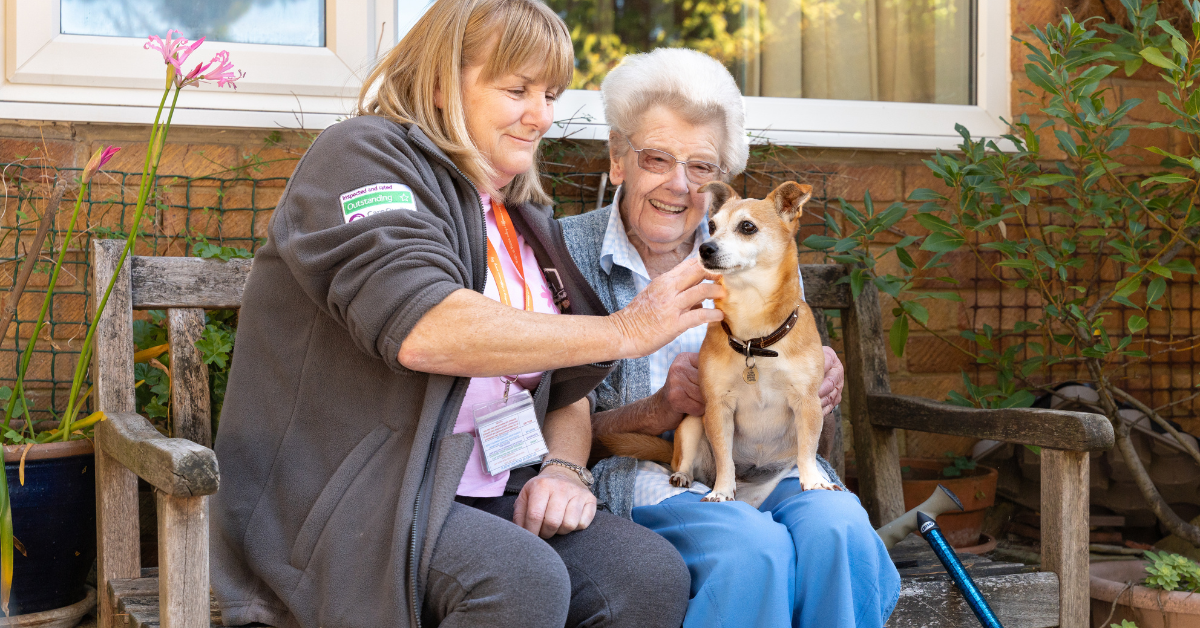 Happy client sitting with her dog and carer, enjoying friendly homecare support.