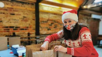 Female wearing Christmas hat and jumper packs paper carrier bags.