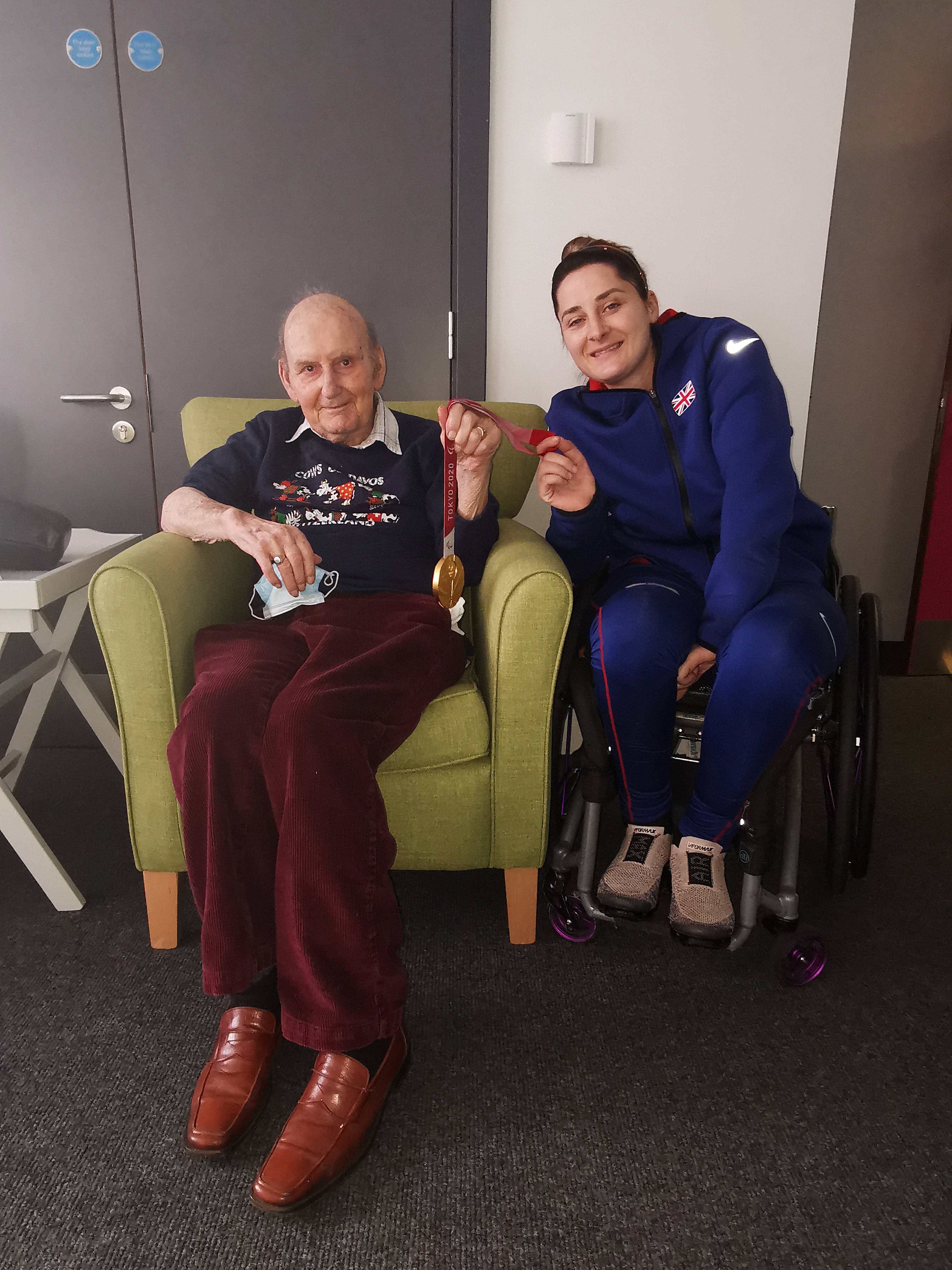 Male sitting armchair and female wheelchair user holding a gold medal on a ribbon
