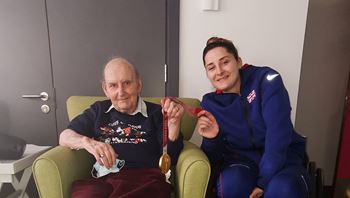 Male sitting armchair and female wheelchair user holding a gold medal on a ribbon