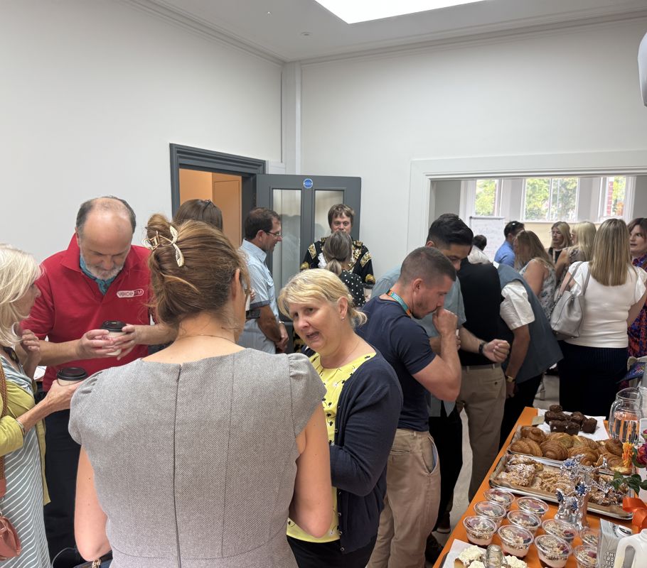 Staff, directors, and guests talking and mingling around the table with food during the opening of the new Right at Home Southampton office